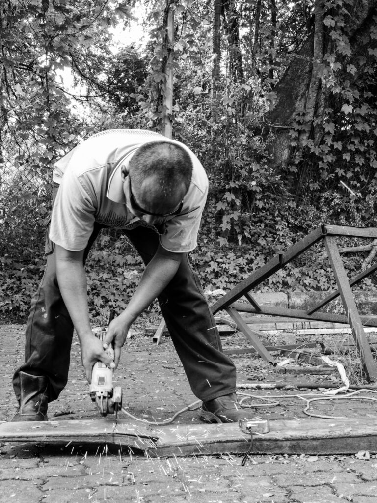 Worker using angle grinder to cut metal outdoors. Worker operates a circular saw in a monochrome outdoor setting in Ipoh, Malaysia.